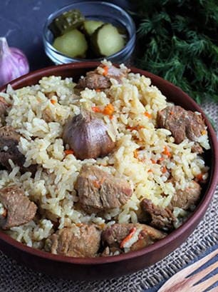 Pilaf with crumbly rice and pork in a cauldron on the stove