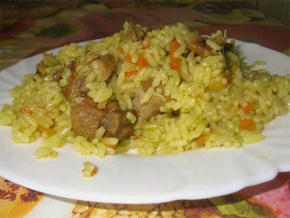 Pilaf with steamed rice and pork in a cauldron on the stove